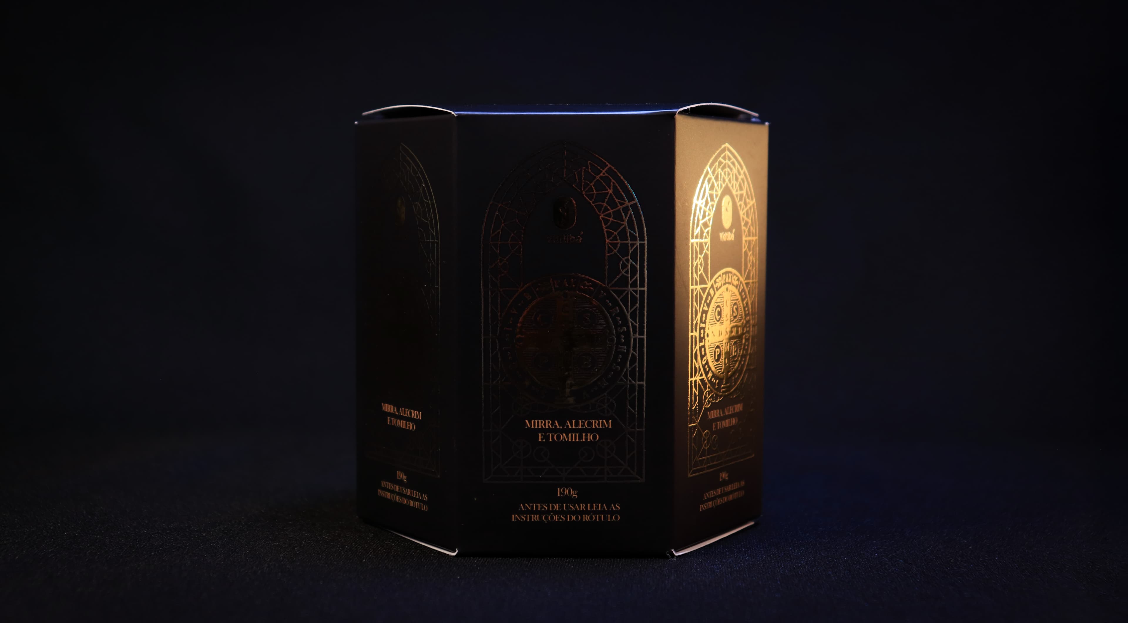 Caixa hexagonal preta aberta como livro, revelando hotstamp dourado em ambas as faces